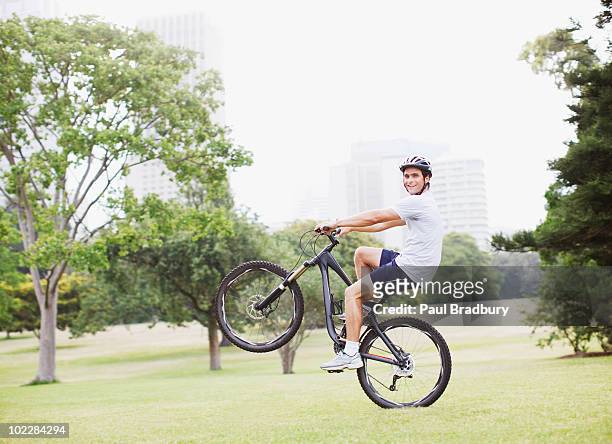man riding bicycle in urban park - wheelie stock pictures, royalty-free photos & images