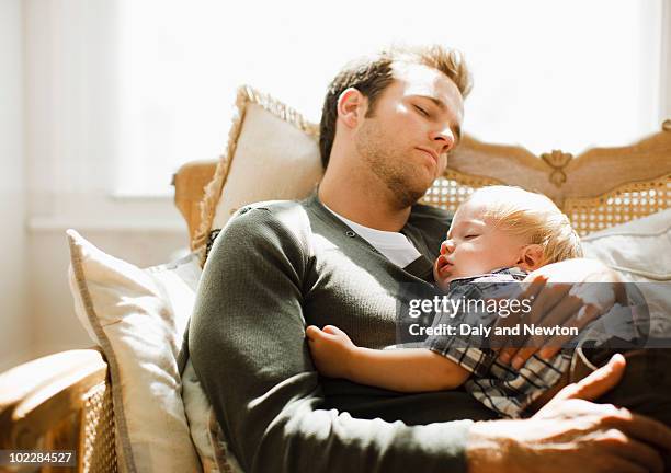 father napping with son on sofa - family serene stock-fotos und bilder