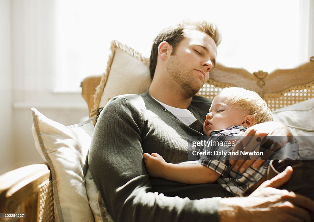 Father napping with son on sofa