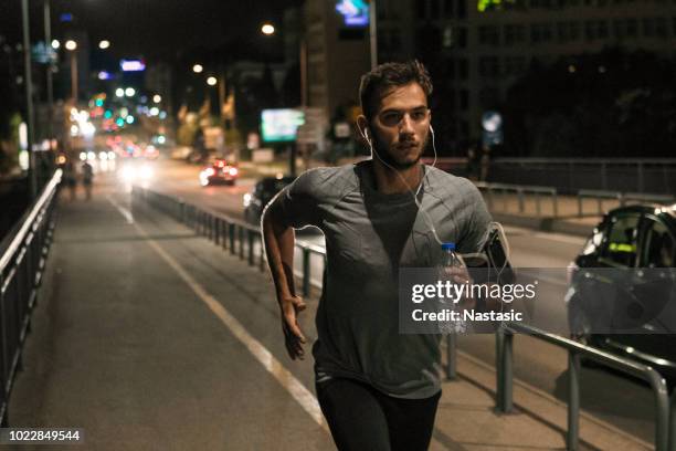 young man jogging through the city at night - track event stock pictures, royalty-free photos & images