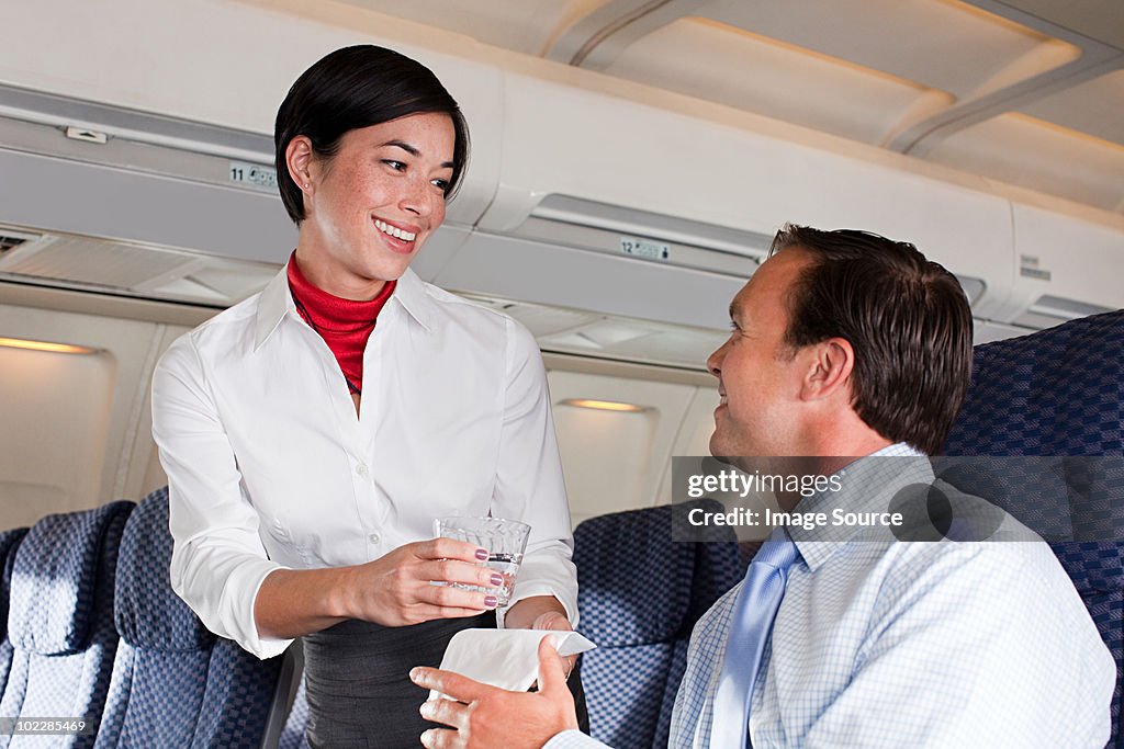 Air stewardess giving drink to passenger