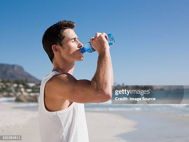 young man drinking water on beach - man drinking water stock pictures, royalty-free photos & images