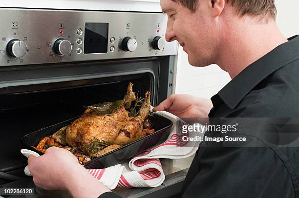 man roasting chicken in oven - mid adult men stock pictures, royalty-free photos & images