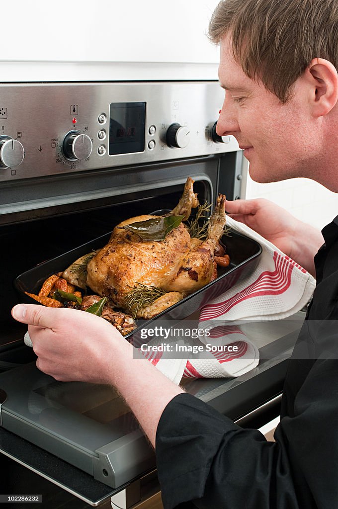 Man roasting chicken in oven