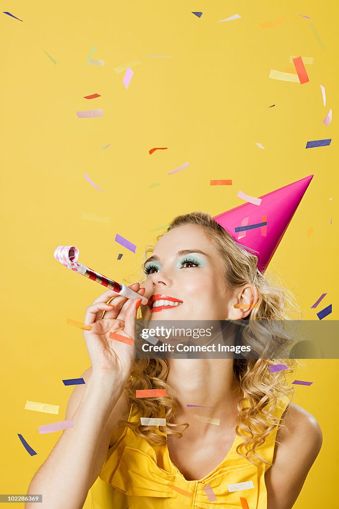 Young woman wearing party hat with party blower and confetti