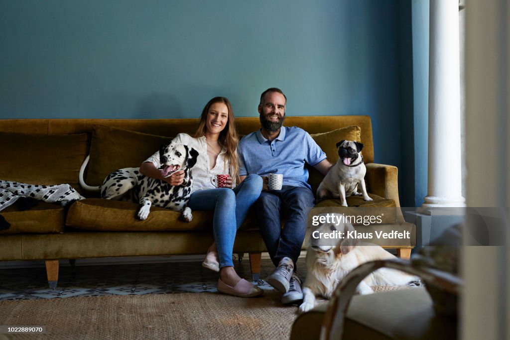 Happy couple sitting in sofa with their 3 dogs