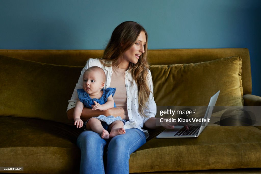 Mother sitting with new born baby and laptop
