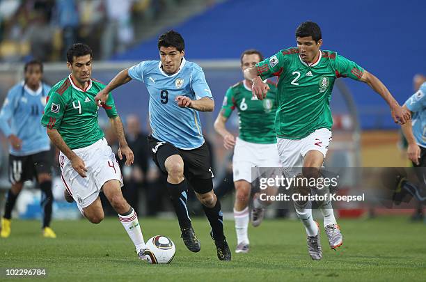 Luis Suarez of Uruguay runs with the ball under pressure from Rafael Marquez and Francisco Rodriguez of Mexico during the 2010 FIFA World Cup South...