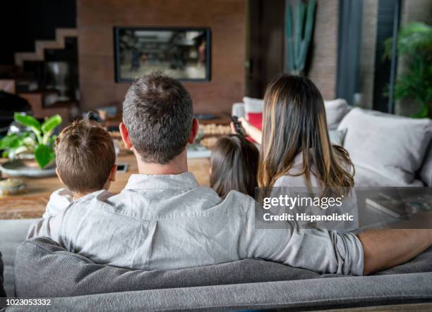 backview van de familie thuis tv-kijken terwijl moeder kanalen verandert - watching tv from behind stockfoto's en -beelden