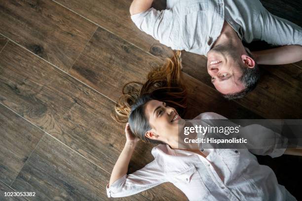 portret van mooie paar liggend op een houten vloer, kijken elkaar lachend - op de rug liggen stockfoto's en -beelden
