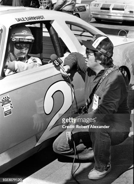 Driver Dale Earnhardt Sr. Is interviewed by a television reporter as he sits in his racecar prior to the start of the 1980 Daytona 500 stock car race...