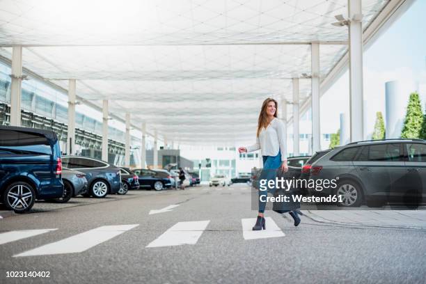 young woman with bag crossing street at zebra crossing - aparcamiento fotografías e imágenes de stock
