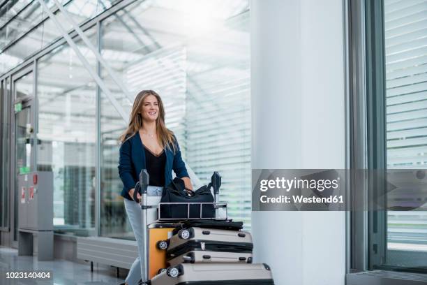 smiling young woman pushing luggage trolley - carrito-para-equipaje fotografías e imágenes de stock