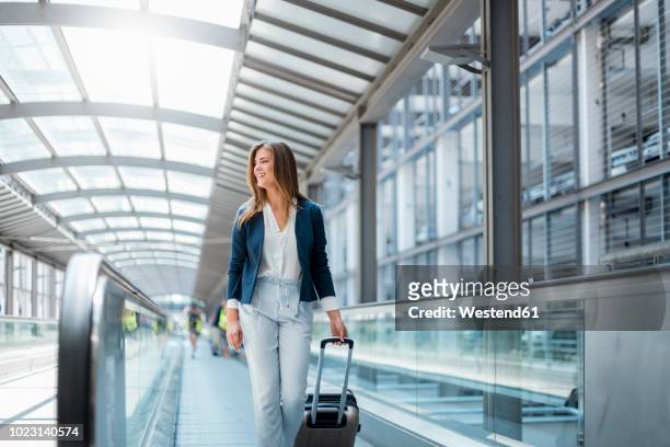smiling young businesswoman with baggage on moving walkway - cinta mecánica fotografías e imágenes de stock