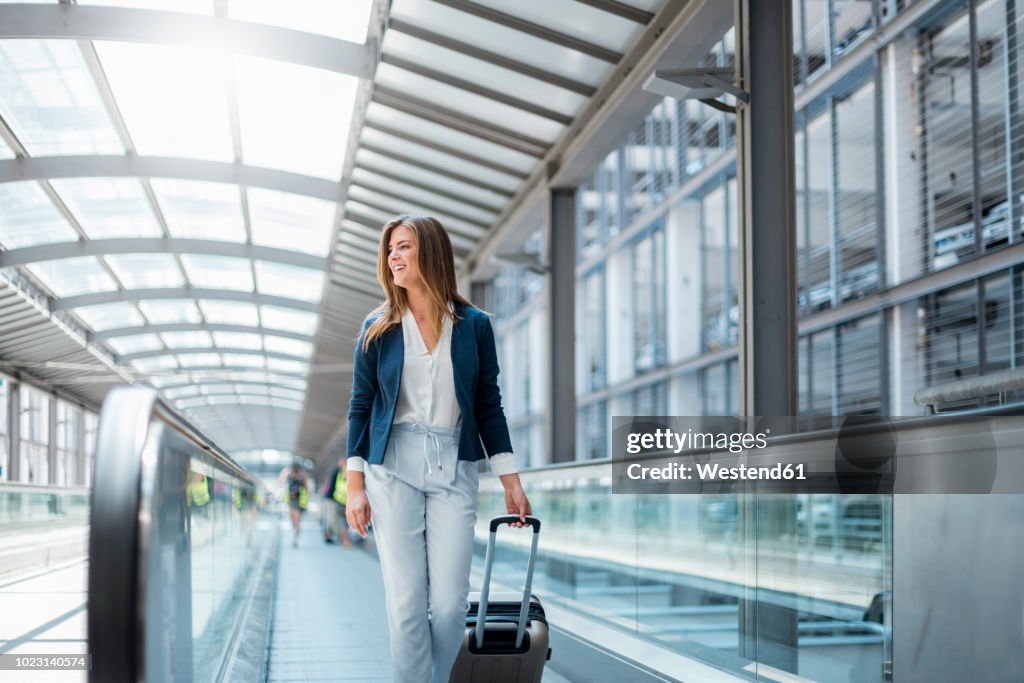 Smiling young businesswoman with baggage on moving walkway