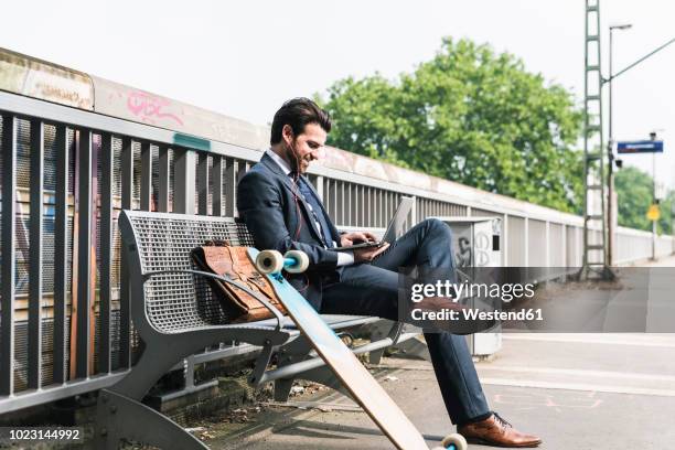 smiling businessman with skateboard using laptop at the platform - arbeiten outdoor stadt laptop stock-fotos und bilder