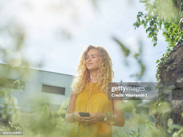 smiling young woman with cell phone and earphones outdoors - yellow dress stock-fotos und bilder