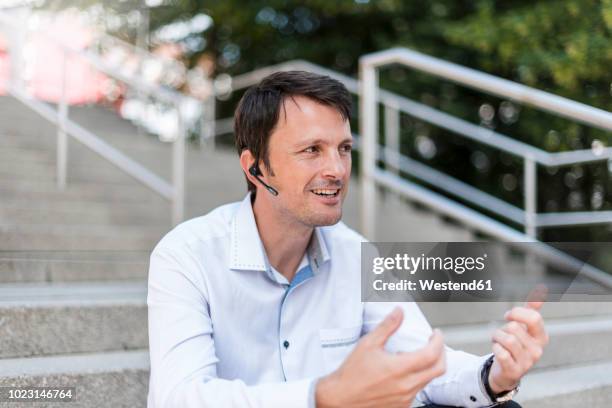 smiling businessman with headset sitting on stairs - bluetooth stock pictures, royalty-free photos & images