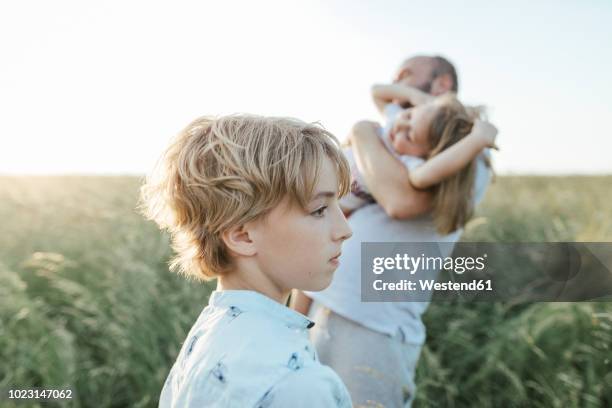 sad boy with father and sister playing together in the background - neid stock-fotos und bilder