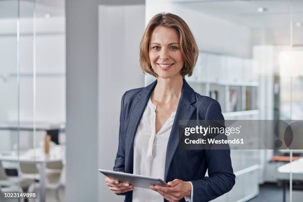 portrait of smiling businesswoman holding tablet in office - geschäftsfrau stock-fotos und bilder