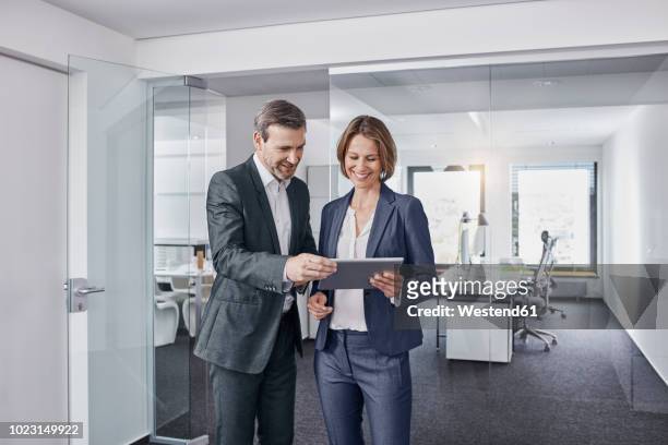 smiling businessman and businesswoman using tablet in office together - tablet 2 personen beratung stock-fotos und bilder