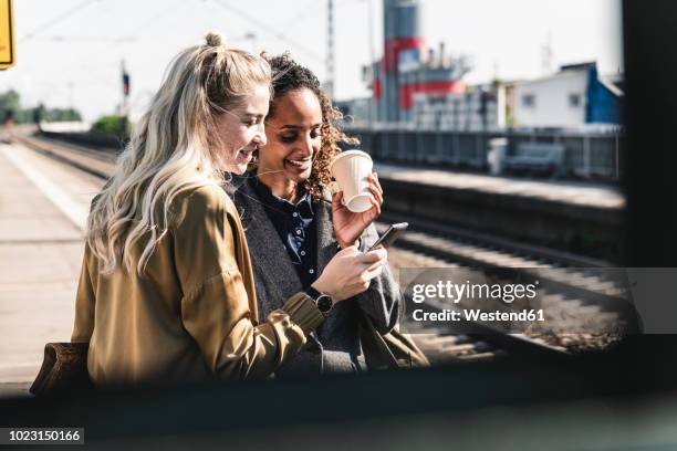 friends waiting at train station looking at smartphone - railway station imagens e fotografias de stock