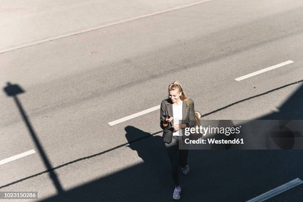 young woman walking on empty road, talking into her smartphone - woman talking cellphone stock-fotos und bilder