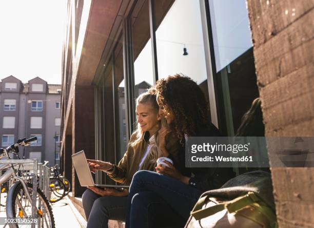 friends sitting in front of window in the city, using laptop - student stock-fotos und bilder