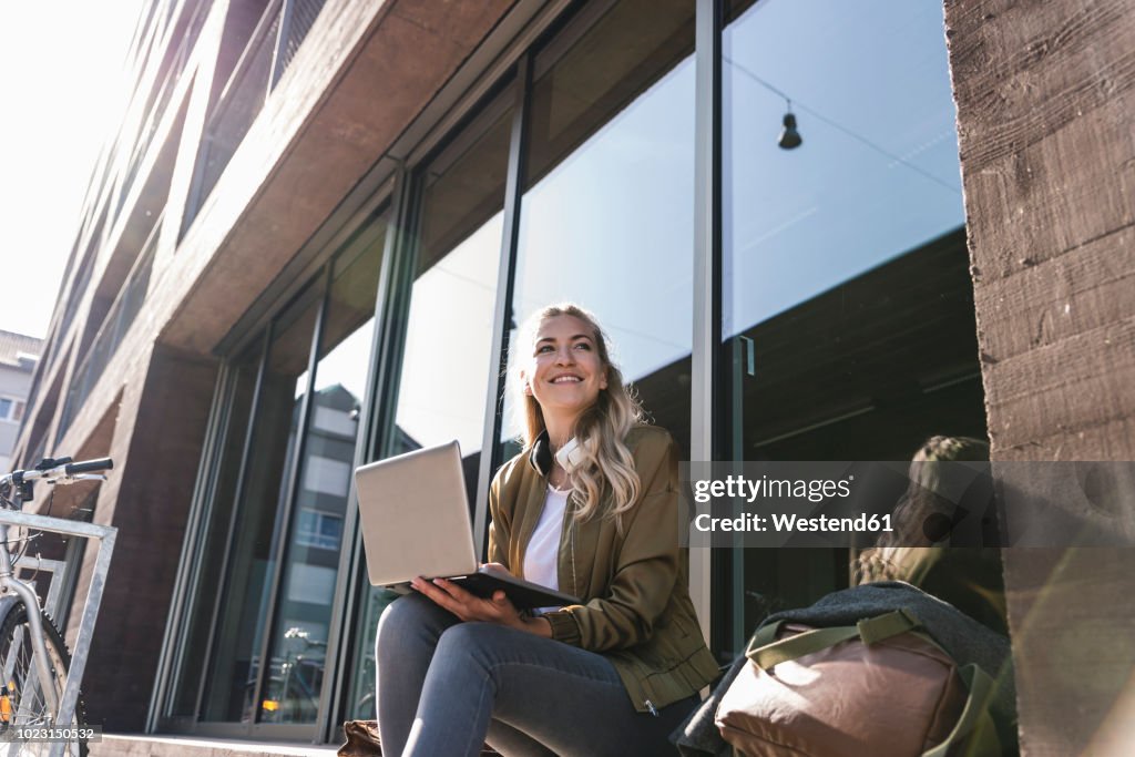 Friends sitting in front of window in the city, using laptop