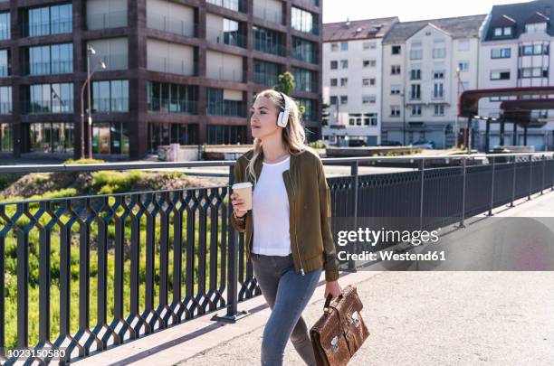young woman walking on bridge, drinking coffee, listening music with headphones - studentessa di scuola secondaria foto e immagini stock