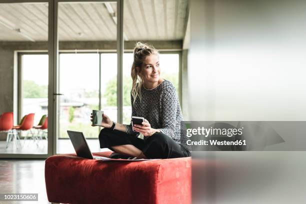 young businesswoman working in modern office, sitting on stool, using laptop - independencia fotografías e imágenes de stock