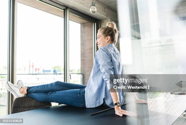 young businesswoman sitting on desk - füße hochlegen stock-fotos und bilder