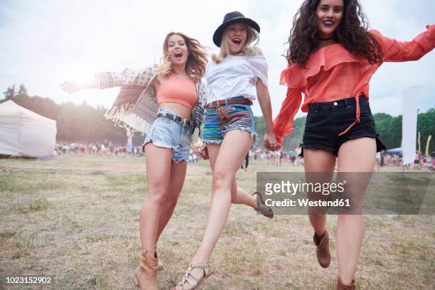 cheerful friends holding hands and running at a music festival - music festival day 3 foto e immagini stock