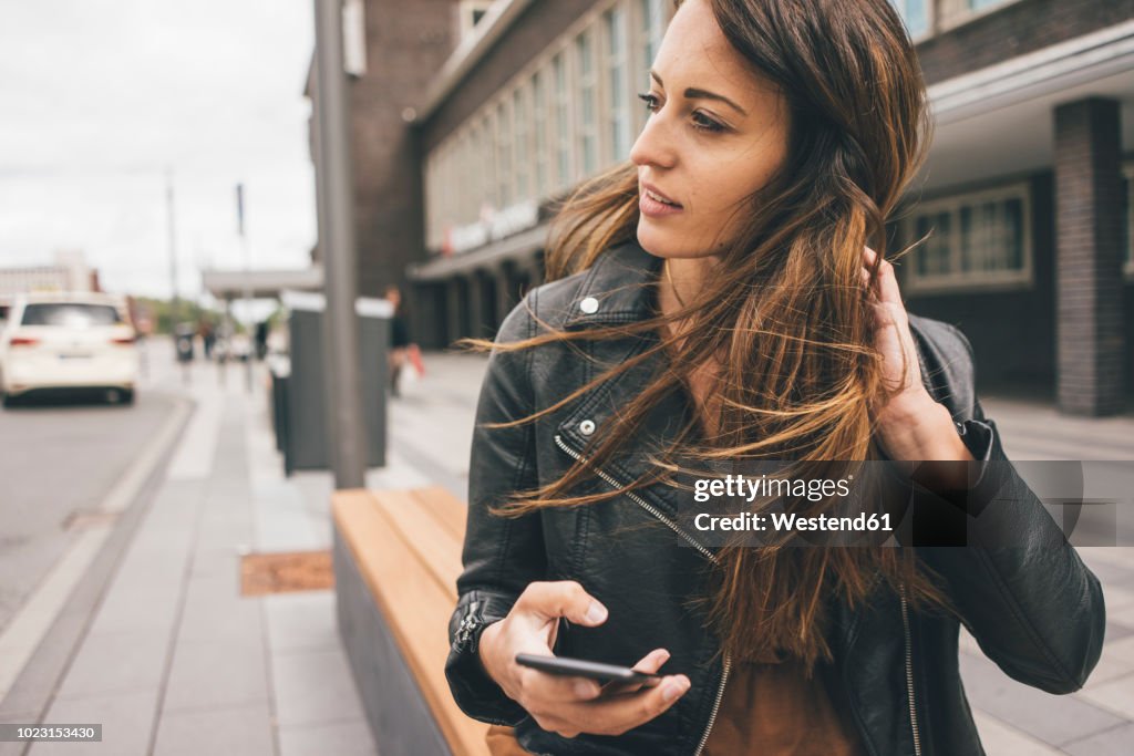 Young woman with windswept hair holding cell phone in the city