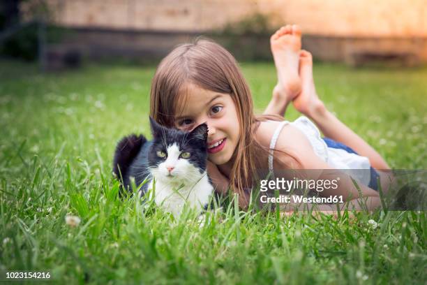 portrait of little girl with cat lying on a meadow - girls cuddling cat stock-fotos und bilder