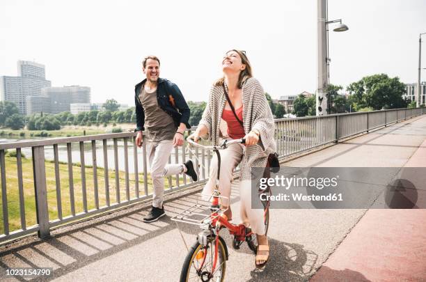 happy couple crossing a bridge with bicycle and by foot - fun couple on bike stock-fotos und bilder