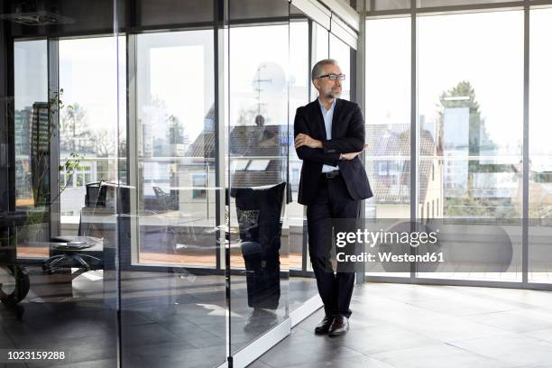 businessman standing in office thinking - business man standing stock-fotos und bilder