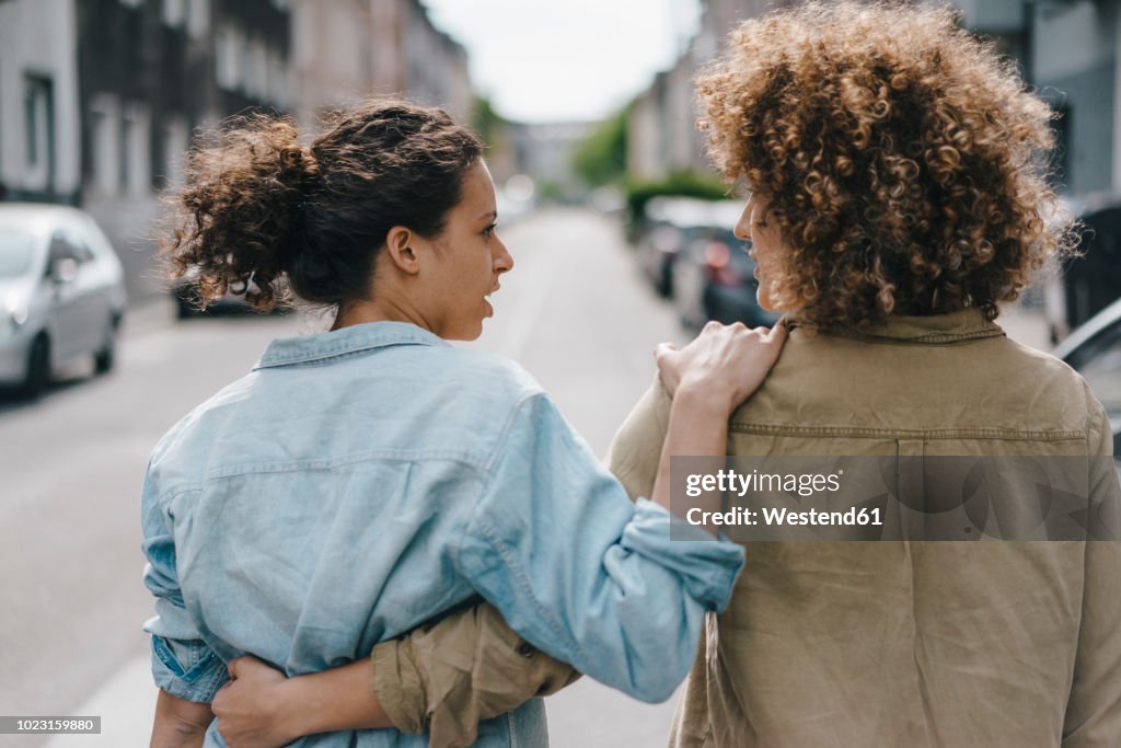 Best friends walking in the city, arm in arm, rear view