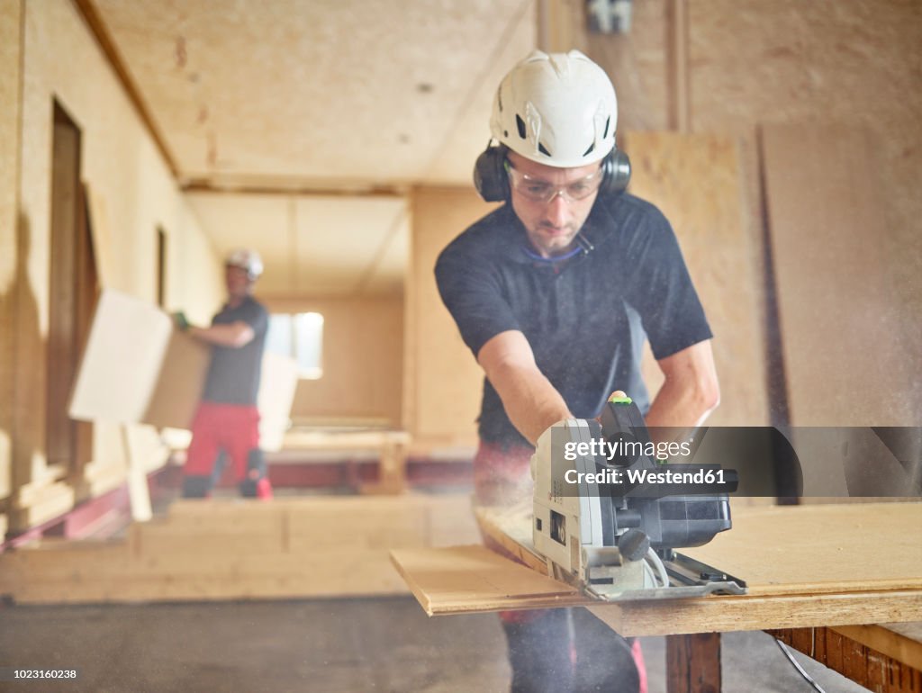 Worker with helmet sawing wood with circular saw