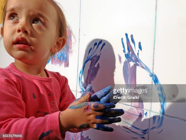 little girl painting the wall with her hands - manos pintadas fotografías e imágenes de stock