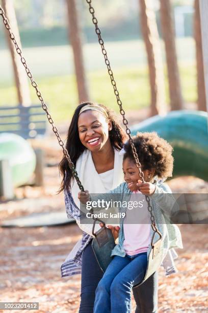 african-american girl with mother at playground on swing - children swinging stock pictures, royalty-free photos & images