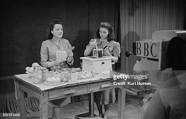 English cookery expert Marguerite Patten supervises pianist Geraldine Peppin as she stirs a pan on the BBC television show 'Designed For Women',...