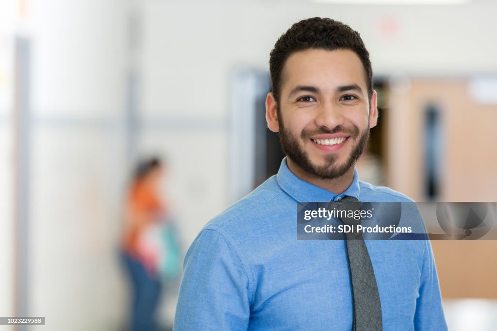 Jovens educador masculino está orgulhosamente no prédio da escola