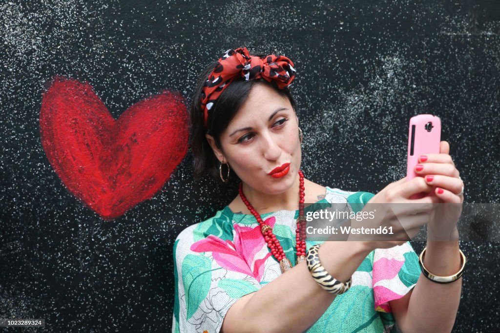 Woman taking a selfie next to heart painted on the wall