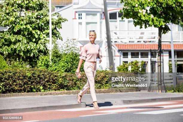 smiling woman crossing a street - korsa bildbanksfoton och bilder
