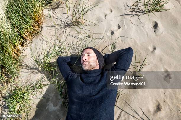 man wearing woolly hat lying in beach dune - man sleeping with cap stock pictures, royalty-free photos & images