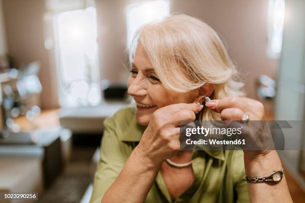 senior woman applying hearing aid - deafness stock pictures, royalty-free photos & images