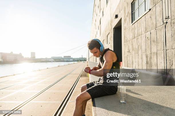 young athlete wearing headphones, sitting on a wall, checking smartwatch - checking watch stock pictures, royalty-free photos & images