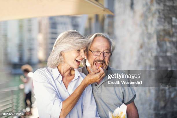 senior couple taking a city break, eating french fries - snacking on the go stock-fotos und bilder