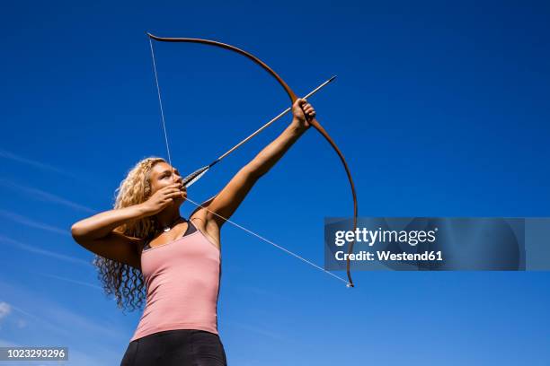 archeress aiming with bow against blue sky - pfeil und bogen stock-fotos und bilder
